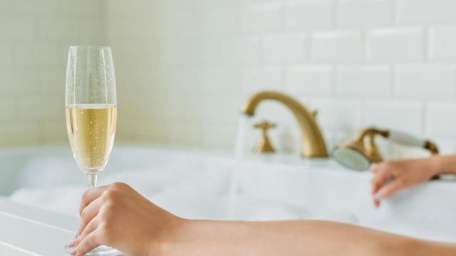 cropped shot of young woman holding glass of champagne in bathtub