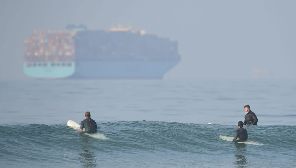 Surfers wait for waves at Huntington Beach, California, as a container ship queues offshore (AFP via Getty Images)