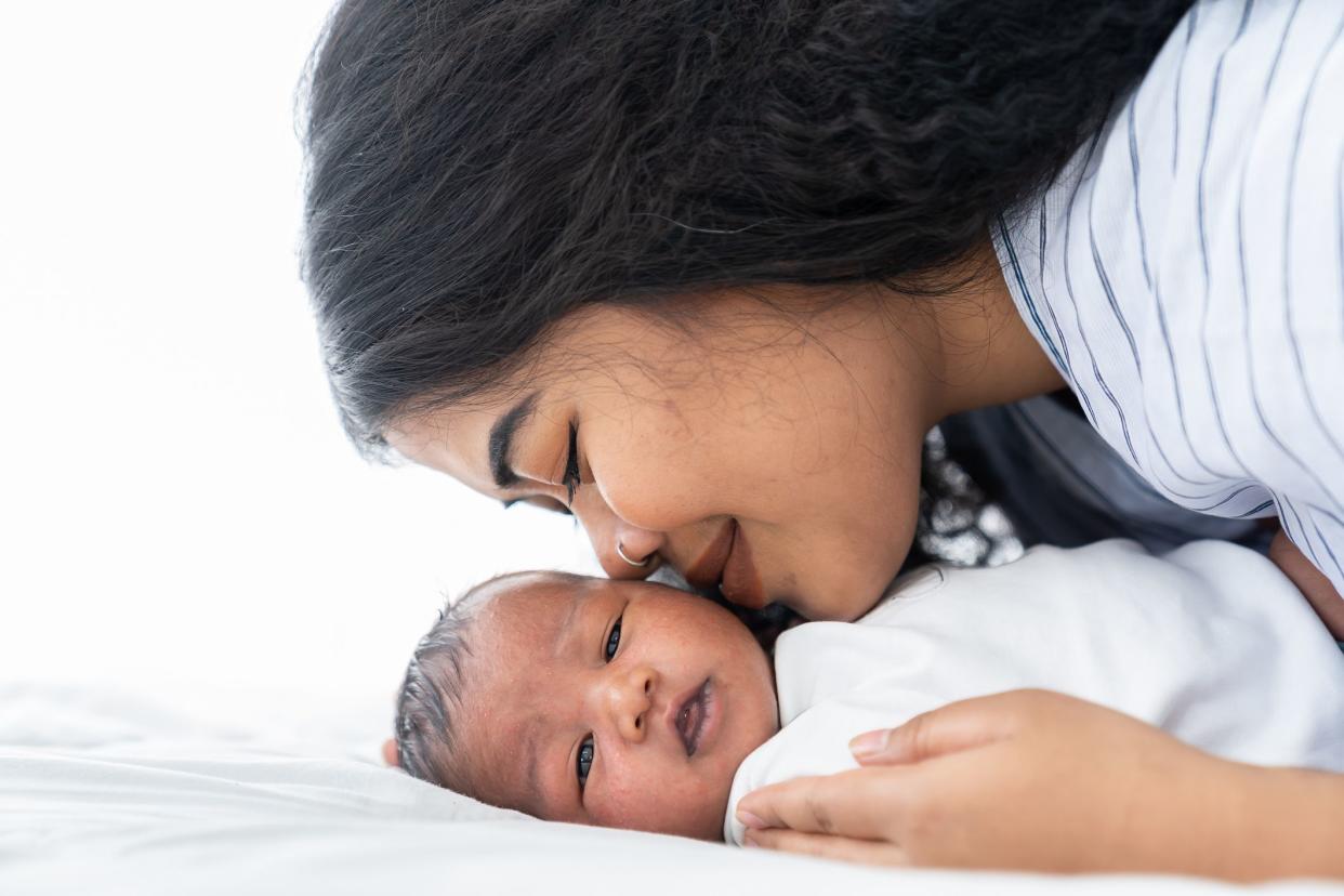 Mother kissing her newborn baby on the bed. Closeup of mom and infant baby