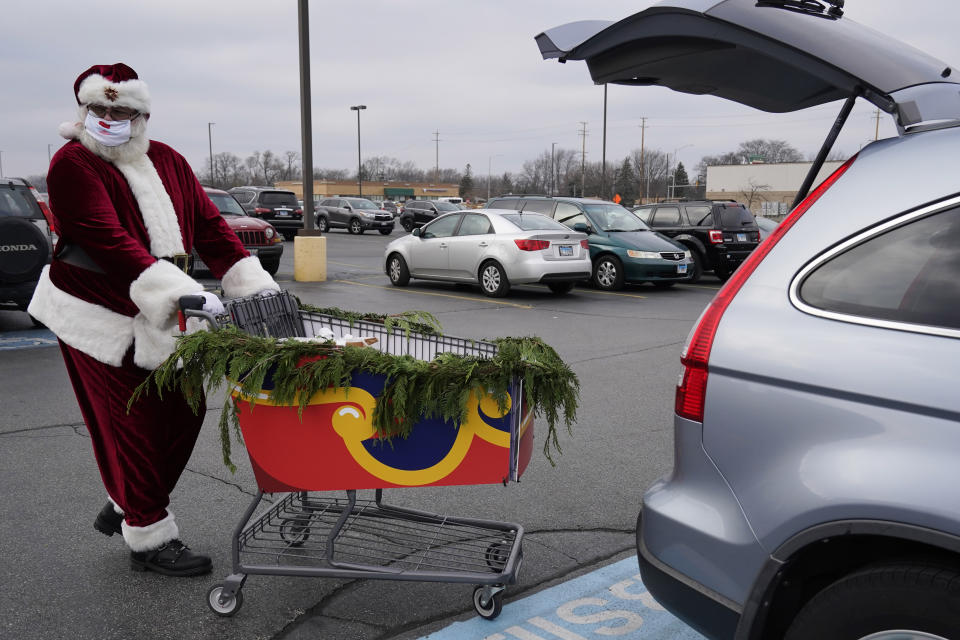 Santa Claus wears a mask as he pushes a sleigh full of curbside grocery orders to an Aldi customer at a parking lot in Palatine, Ill., Saturday, Dec. 19, 2020. For this weekend only, Santa Claus is delivering groceries to Aldi customers in Palatine and several other towns in the Chicago area. (AP Photo/Nam Y. Huh)