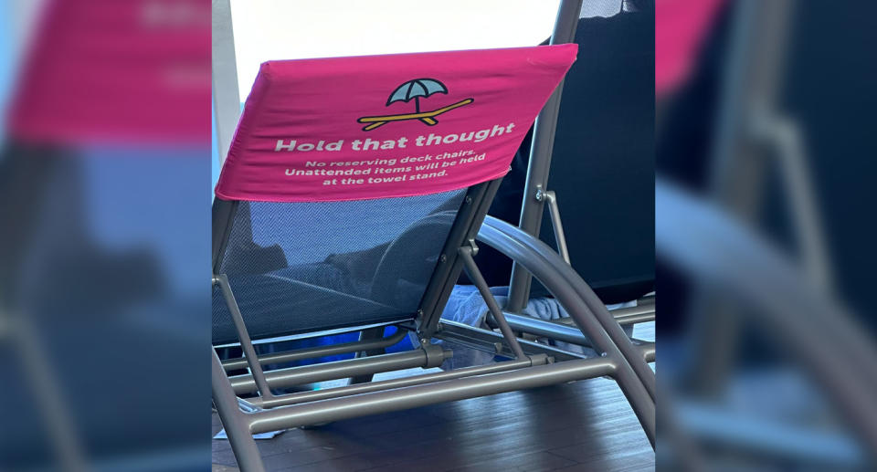 The pool chair has a pink cover over it which reads 'Hold That Thought. No reserving deck chairs. Unattended items will be held at the towel stand.'