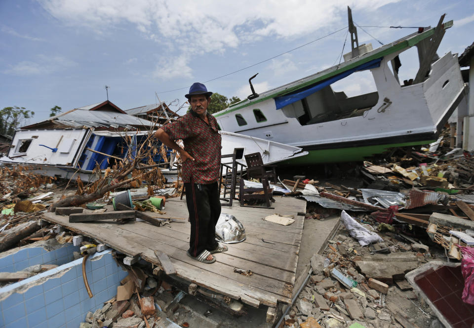 In this Oct. 4, 2018, photo, a man stands amid the damage near boats swept ashore by the tsunami in Wani village on the outskirts of Palu, Central Sulawesi, Indonesia. People living in tents and shelters have little but uncertainty since the powerful earthquake and tsunami hit the city, where death toll rises and efforts to retrieve scores more victims buried deep in mud and rubble were still hampered Thursday by the lack of heavy equipment. (AP Photo/Dita Alangkara, File)