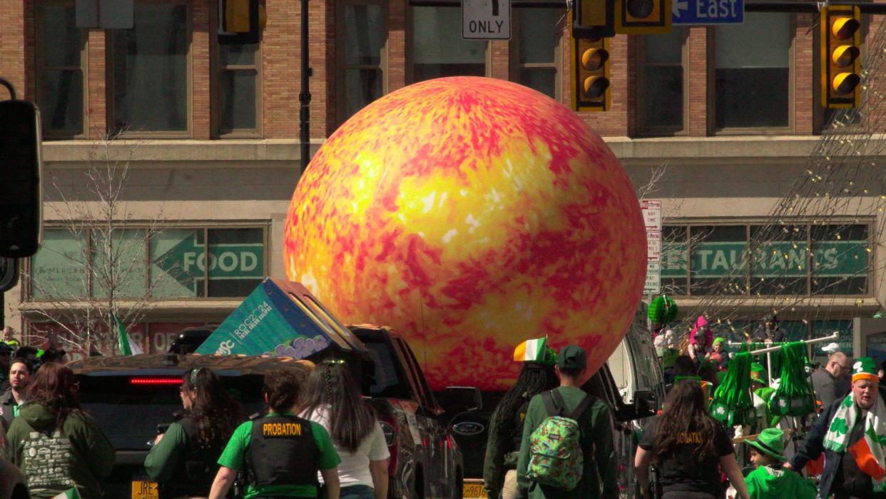 A large ball resembling the sun gets folks read for the April 8th solar eclipse during the St. Patrick's Day parade in downtown Rochester.