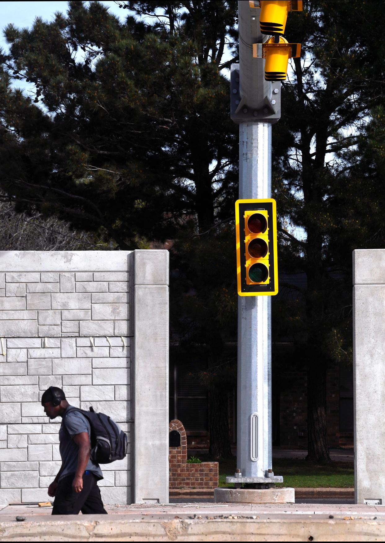 A pedestrian passes a traffic signal occupying a break in the new wall separating Buffalo Gap Road from homes on Flintlock Dr. in south Abilene Wednesday March 20, 2024.