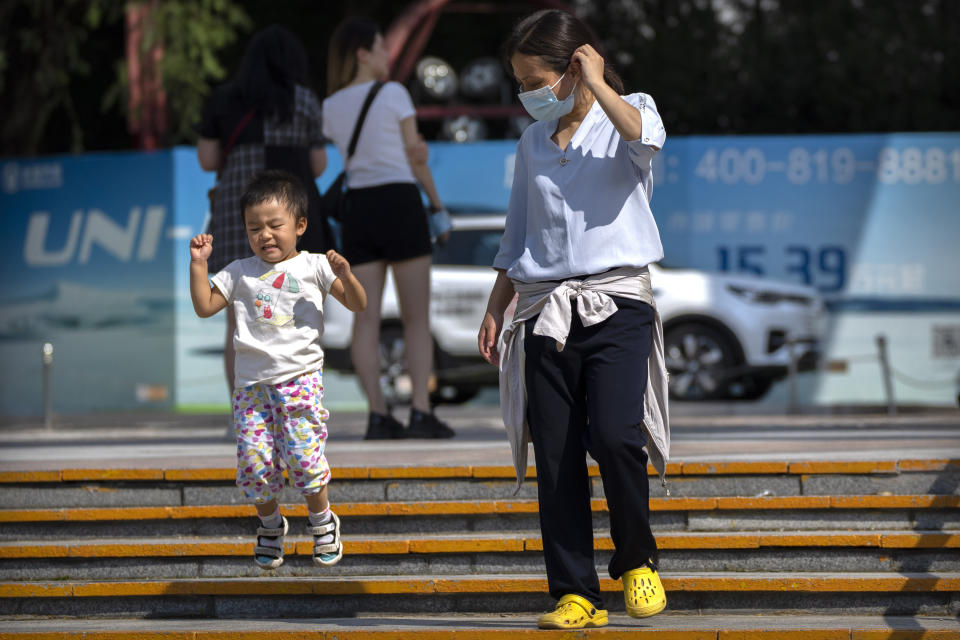 A woman watches as a child jumps down steps at a public park in Beijing, Saturday, Aug. 21, 2021. China will now allow couples to have a third child as the country seeks to hold off a demographic crisis that threatens its hopes of increased prosperity and global influence. (AP Photo/Mark Schiefelbein)