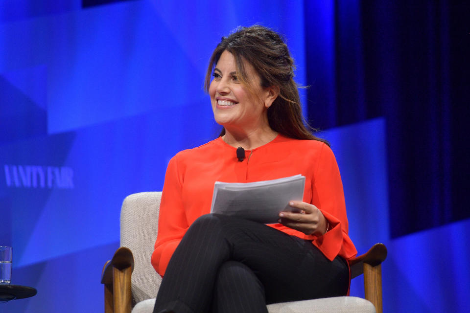 Lewinsky smiles while sitting in a chair and holding a sheath of papers