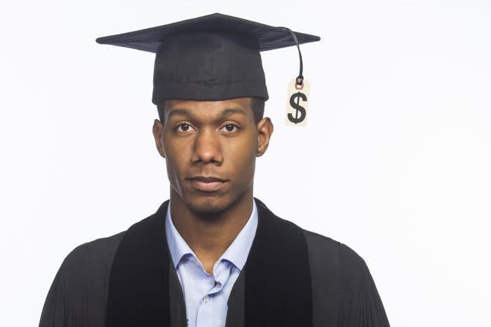 College graduate in cap and gown with dollar sign hanging from tassel.