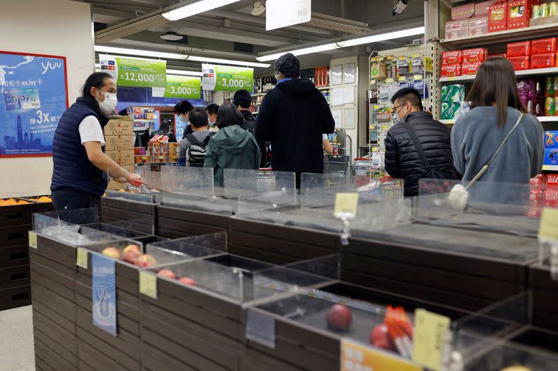 Customers wearing masks shop in front of partially empty shelves at a supermarket in Hong Kong