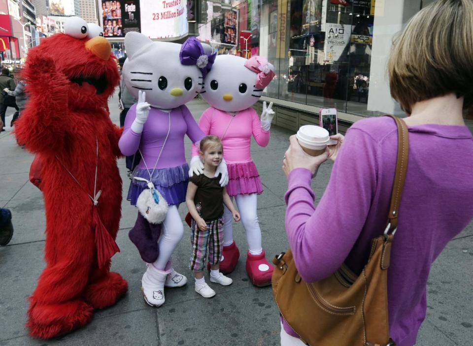 Elmo and two Hello Kitty characters pose for photos with a little girl in New York's Times Square, Tuesday, April 9, 2013.  A string of arrests in the last few months has brought unwelcome attention to the growing number of people, mostly poor immigrants, who make a living by donning character outfits, roaming Times Square and charging tourists a few dollars to pose with them in photos. (AP Photo/Richard Drew)