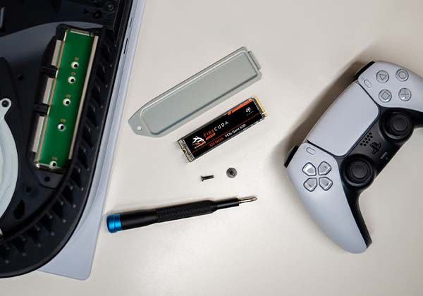 a ps5 console torn down to expose the expansion ssd slot while an ssd, screwdriver, and ps5 controller sit next to the console