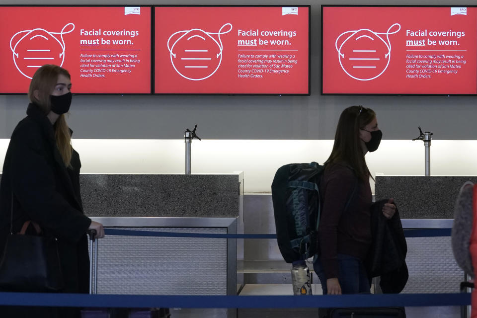 FILE— In this Dec. 22, 2020 file photo, signs advising facial covering requirements are shown as travelers stand in line at a Delta Air Lines desk at San Francisco International Airport during the coronavirus pandemic in San Francisco. Health officials in San Francisco and six other Bay Area counties announced Monday, Aug. 2, 2021 that they are reinstating a mask mandate for all indoor settings as COVID-19 infections surge because of the highly contagious delta variant. (AP Photo/Jeff Chiu, File)