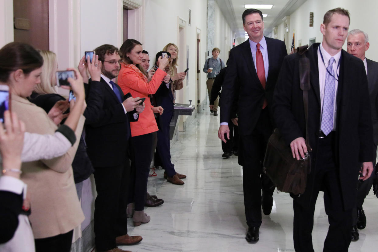 U.S. former FBI Director James Comey walks, smiling, down a corridor toward a House hearing.