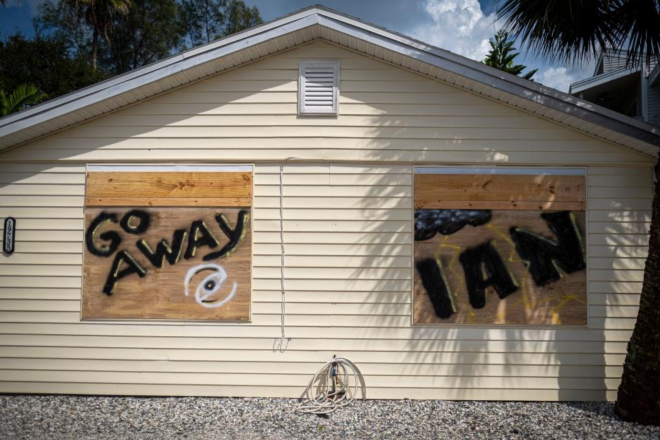 A house with the windows covered with wood boards spray-painted with the words: Go away and Ian