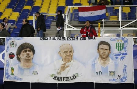 A Chile fan stands behind a banner depicting (L-R) retired Argentina soccer player Diego Maradona, Pope Francis and Argentina's Lionel Messi as he awaits the start of the Copa America 2015 semi-final soccer match between Argentina and Paraguay at Estadio Municipal Alcaldesa Ester Roa Rebolledo in Concepcion, Chile, June 30, 2015. REUTERS/Andres Stapff