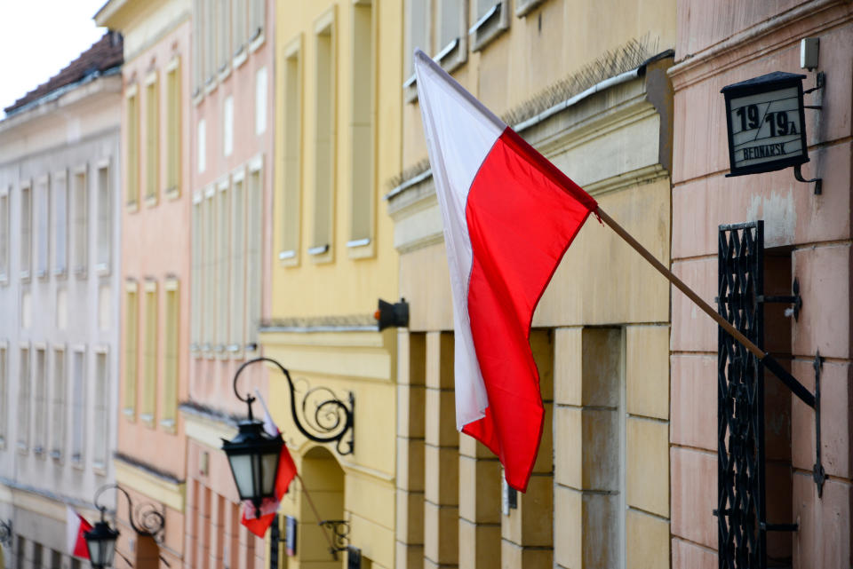 The national flag of Poland displayed on poles outside traditional buildings in the old town of Warsaw