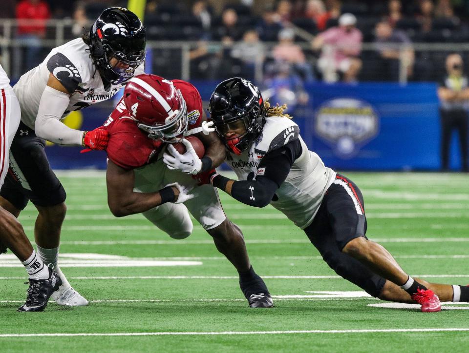 Cincinnati Bearcats linebacker Deshawn Pace (20) left, and  safety Bryan Cook (6), right, take down Alabama Crimson Tide running back Brian Robinson Jr. (4) during the College Football Playoff Semifinal at the 86th  Cotton Bowl Classic Friday December 31, 2021 at AT & T Stadium in Arlington, Texas.