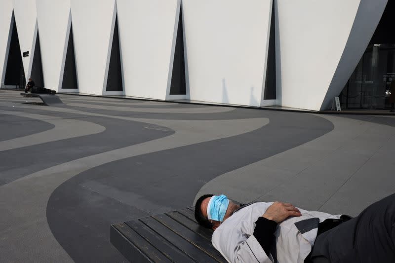 A man wears his protective mask over his eyes as he sleeps on a bench after outbreaks of the coronavirus disease (COVID-19) in Beijing