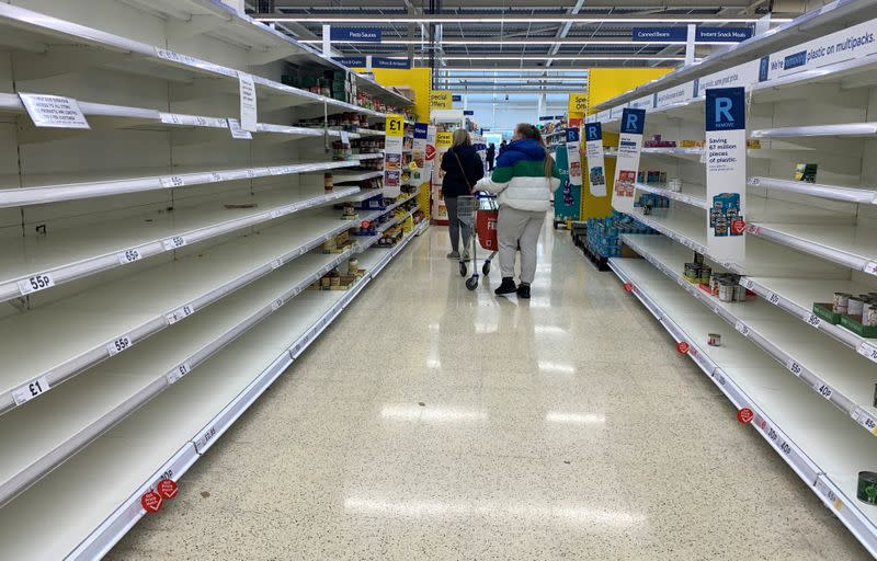 Shoppers walk past empty shelves inside a Tesco supermarket in Liverpool