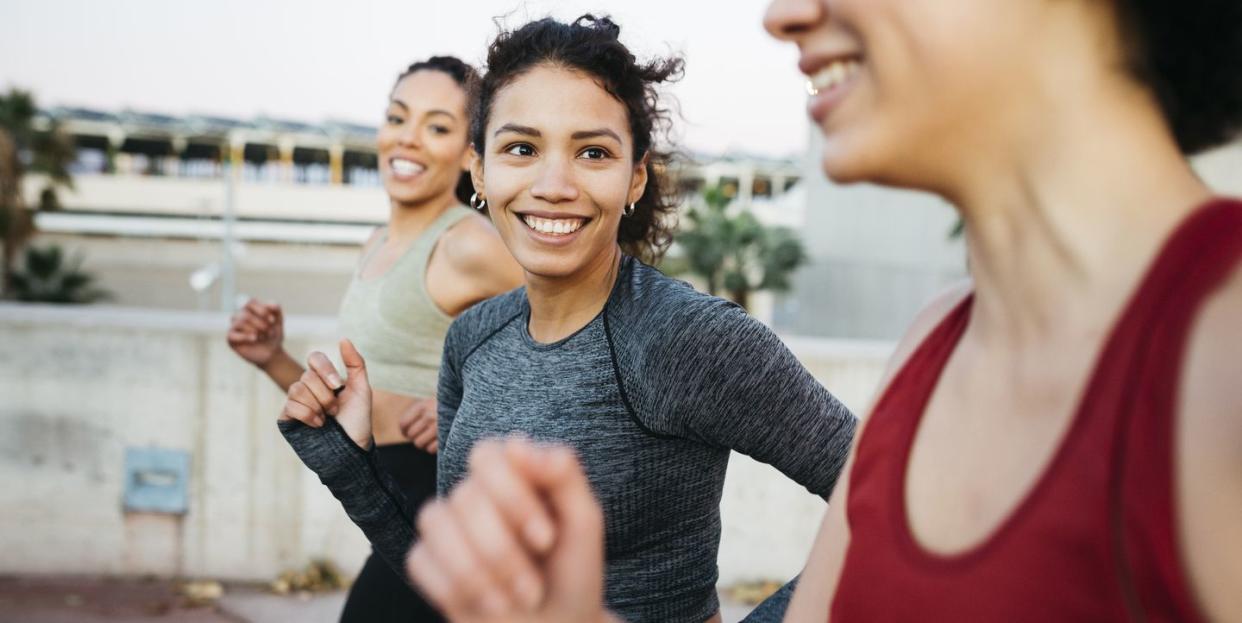 three smiling young women, wearing sports clothes, jogging on an urban scenario