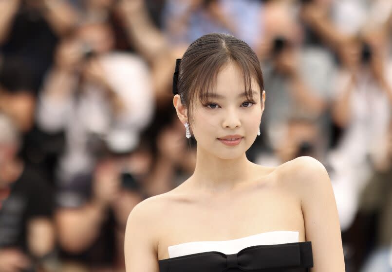 Blackpink's Jennie poses in a sleeveless black-and-white dress and diamond earrings with a crowd blurred out behind her.