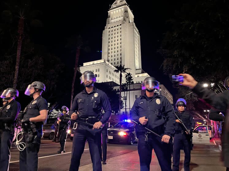 Los Angeles Police Officers stand outside their department as crowds block Main and First Streets in downtown Los Angeles late Friday evening