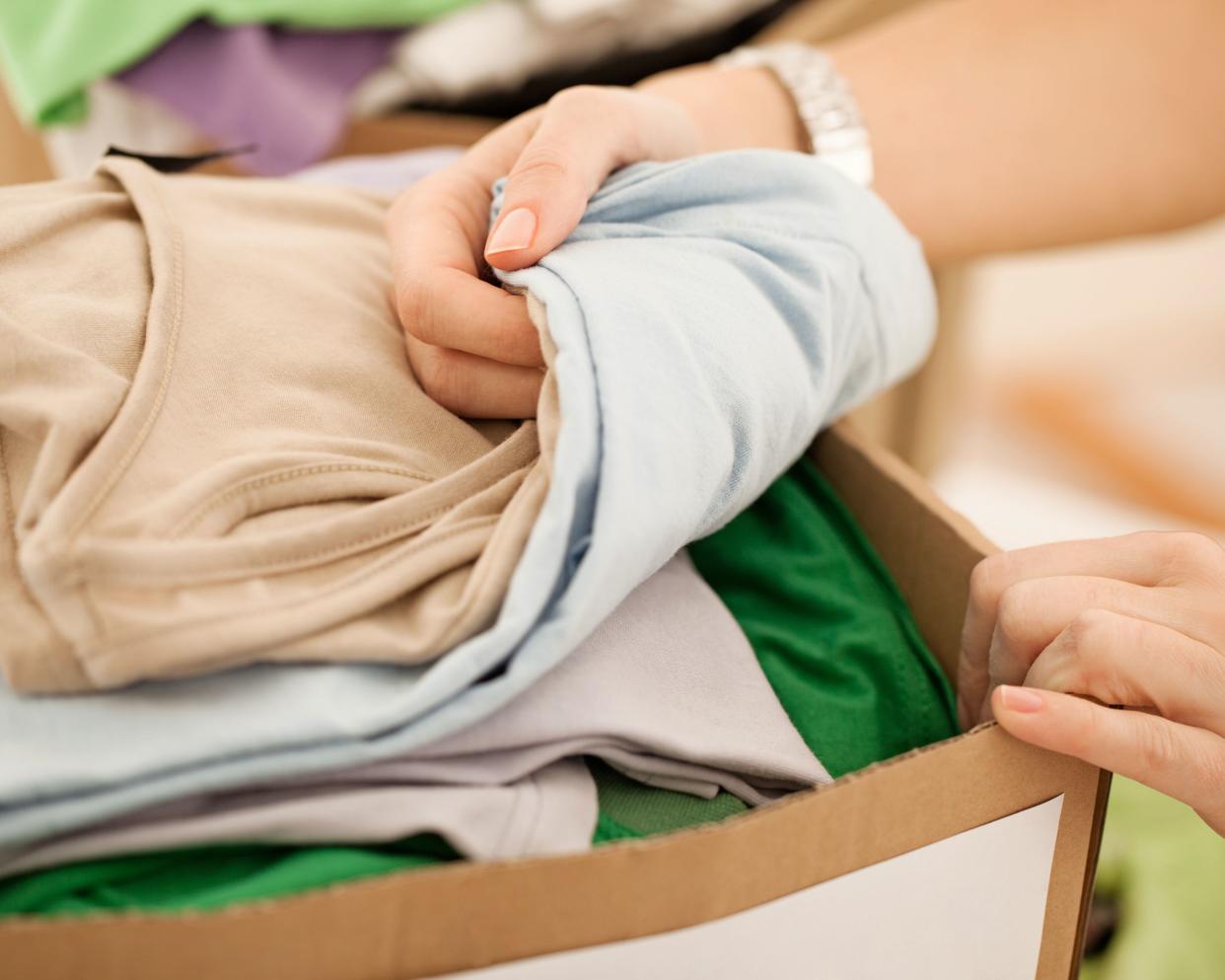 Woman's hand over stack of clothes in box