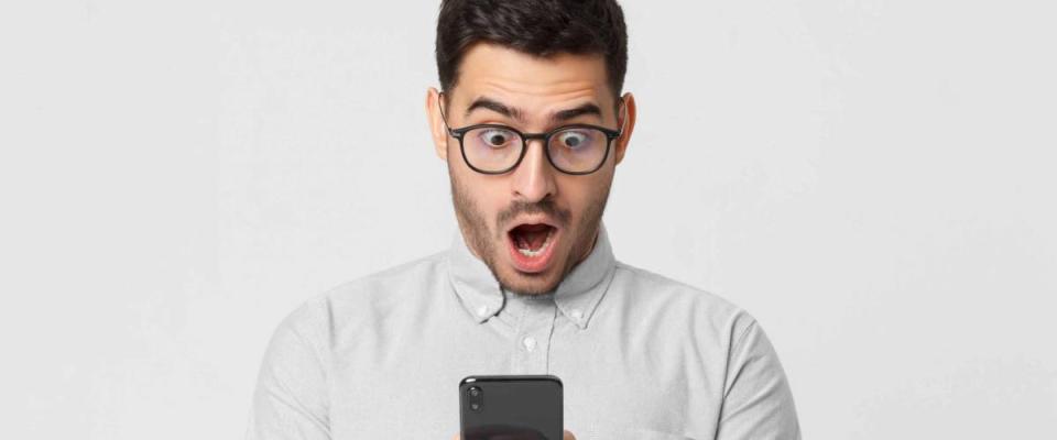 Shocked business man in casual shirt looking at his phone with surprise expression, isolated on gray background