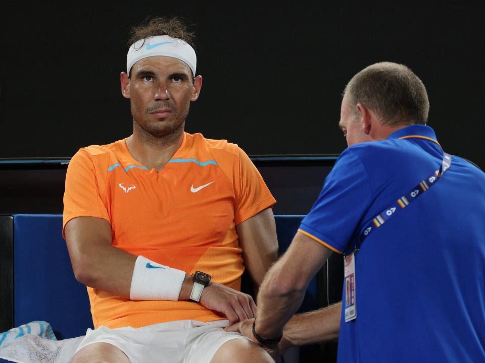 Rafael Nadal winces as a medical staffer treats his injured hip.