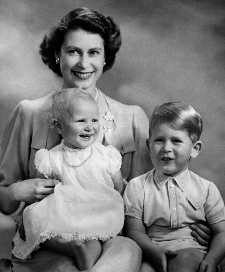 Princess Anne sits in her mother's lap next to Prince Charles