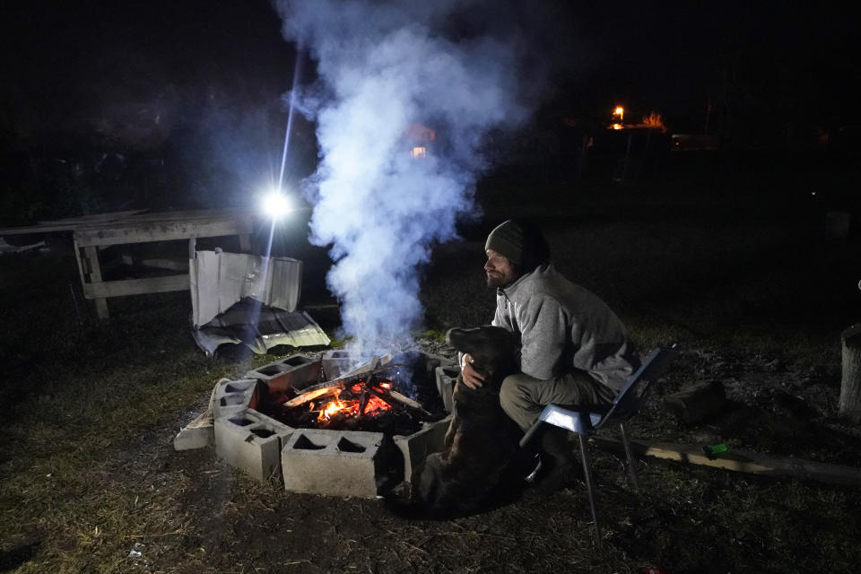 Ricky Trahan sits next to a fire with one of his dogs on Christmas Eve night, while his wife stays inside the tent they now live in, amidst the rubble of their destroyed home in the aftermath of Hurricane Laura and Hurricane Delta, in Lake Charles, La., Thursday, Dec. 24, 2020. The family is living in tents with one son, while another son, his fiancee and their one-year-old son is living in a loaned camper there. His sister's family's home is now gutted and they are living in a camper on the same property. (AP Photo/Gerald Herbert)