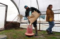 Ward refills a chicken feeder as his wife looks over the chicken house on their farm in Pawnee