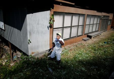 A local resident pauses as he pulls out the weeds at an empty house in Nanmoku Village, northwest of Tokyo, Japan October 12, 2017. REUTERS/Issei Kato