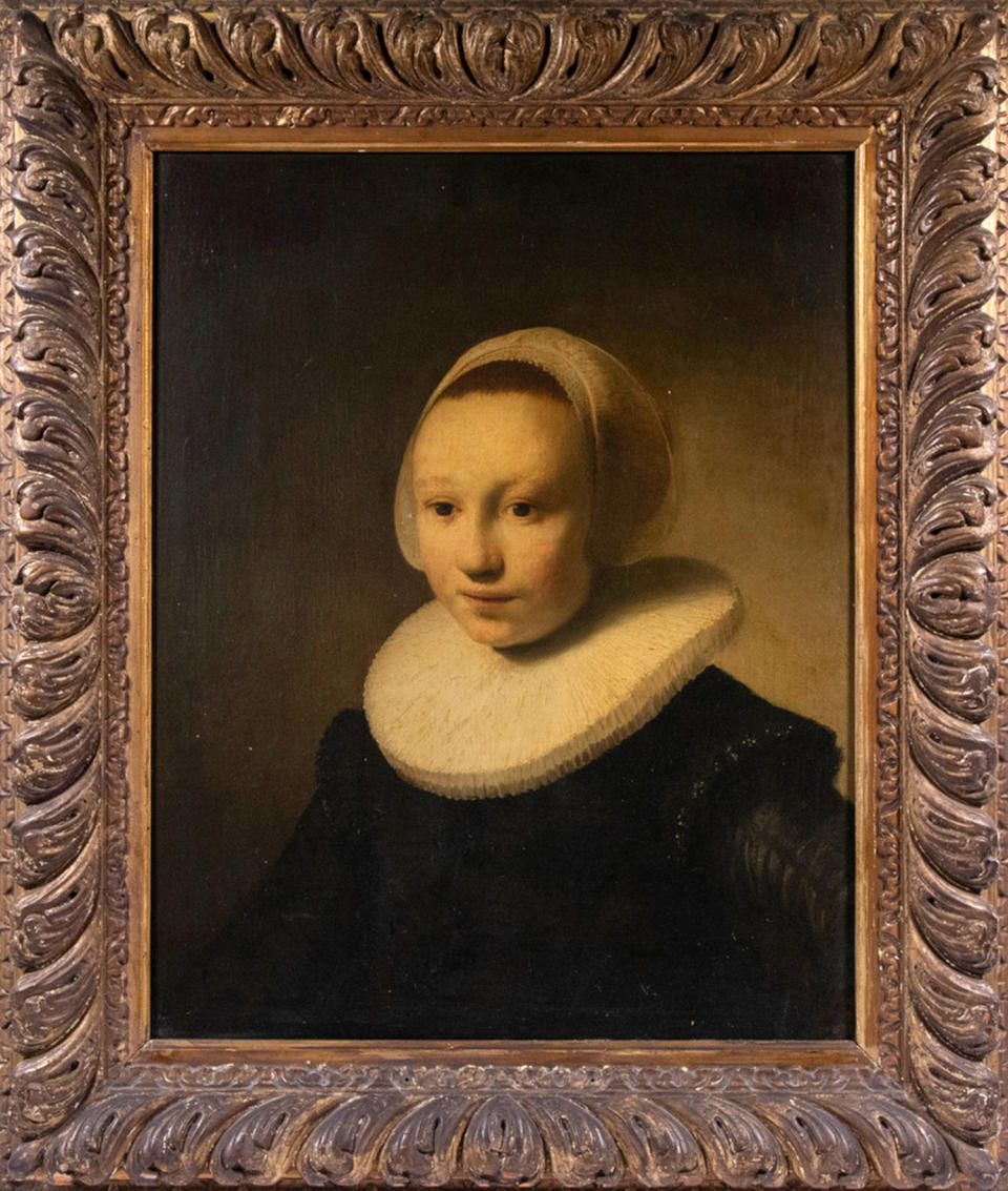 A painting of a girl wearing a black dress, a white headwrap, and a white ruff around her neck, with a brown background and wooden frame around the exterior (Thomaston Place Auction Galleries via AP)