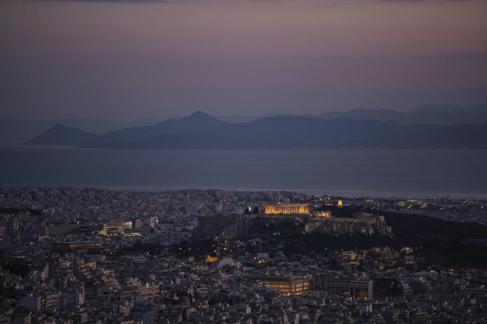 The Acropolis is lit as the island of Aegina stands in the background and behind it the distant shores of the Peloponnese peninsula Friday, April 24, 2020 in Athens. (AP Photo/Petros Giannakouris)