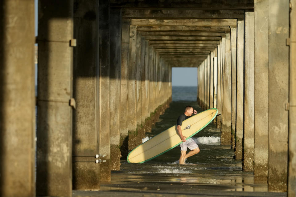 A surfer passes under a pier after spending time in the water ahead of Beryl's arrival, Saturday, July 6, 2024, in Port Aransas, Texas. (AP Photo/Eric Gay)