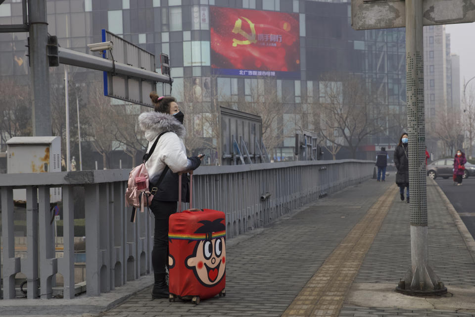 A traveler stands on a bridge near a display showing government propaganda in the fight against the COVID-19 viral illness in Beijing, China Thursday, Feb. 13, 2020. China is struggling to restart its economy after the annual Lunar New Year holiday was extended to try to keep people home and contain novel coronavirus. Traffic remained light in Beijing, and many people were still working at home. (AP Photo/Ng Han Guan)