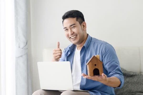 Asian man holding house in his hand and using laptop, real estat