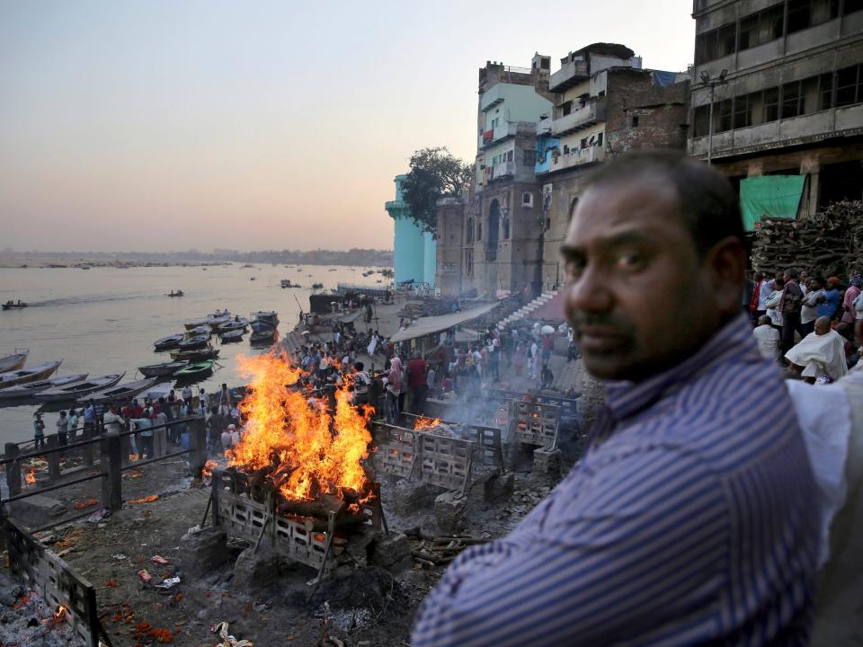 A man looks into the camera as funeral pyres burn in the background on the banks of river Ganges, in Varanasi, India.