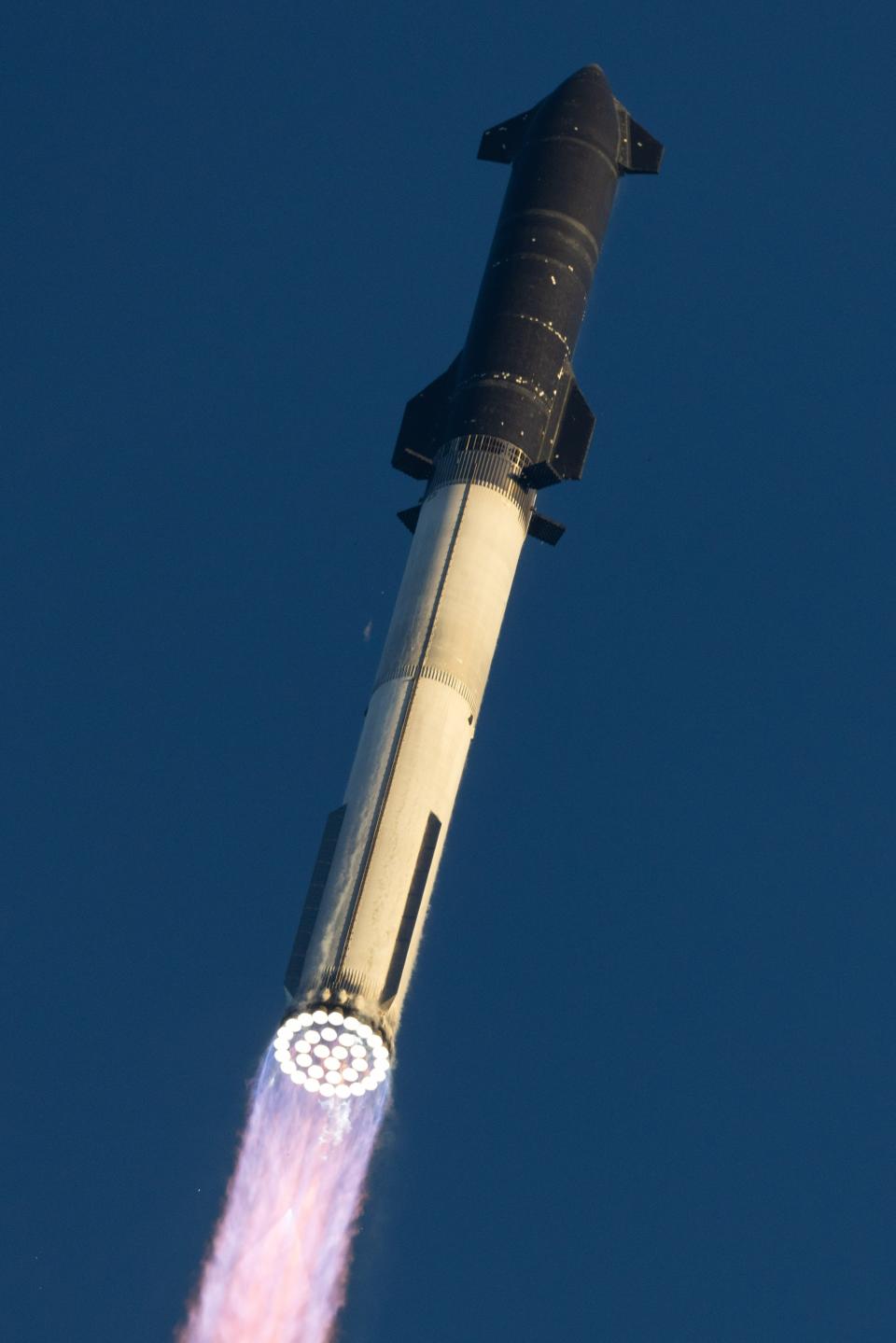 a large black and silver rocket is launched into a clear morning sky