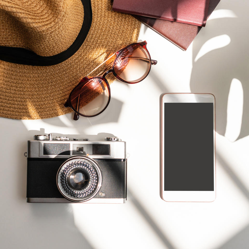 a camera, phone, sunglasses, and a hat on a table