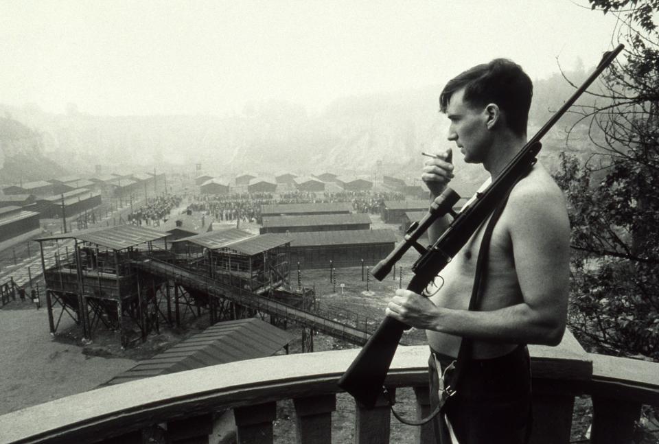 Goeth holding a sniper rifle while looking over a Nazi work camp