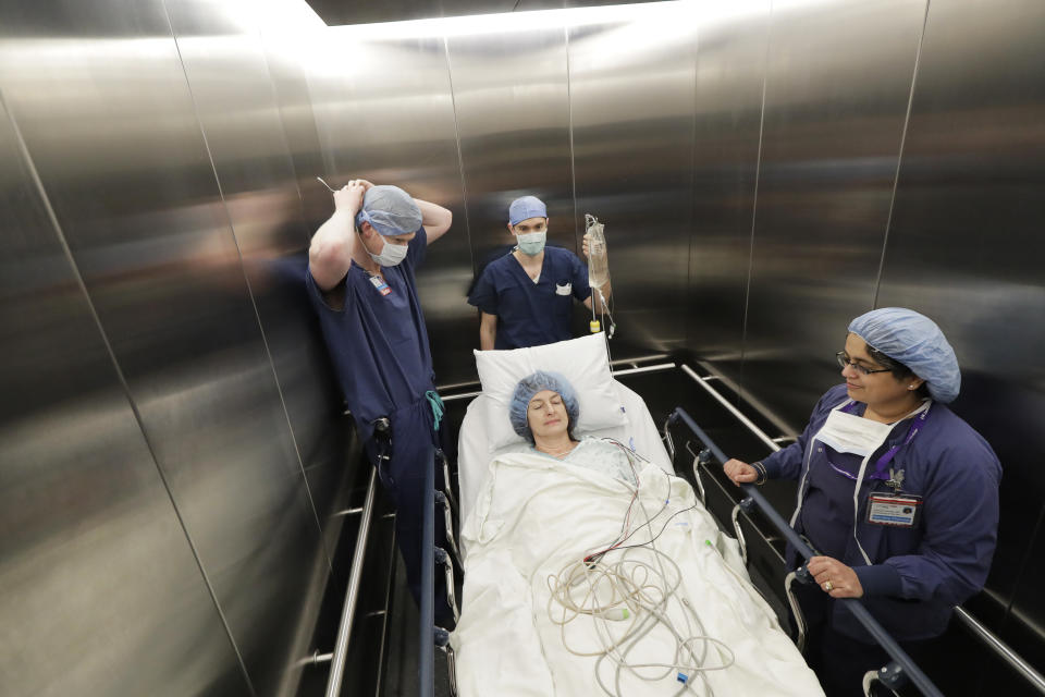 In this Jan. 14, 2020 photo, Genette Hofmann, center, is transported in an elevator by medical staff at Harborview Medical Center in Seattle just before undergoing brain surgery in hopes of reducing the epileptic seizures that had disrupted her life for decades. At the same time, Hofmann agreed to donate a small bit of her healthy brain tissue to researchers. The decision to contribute to the study was simple, even beyond her own epilepsy. She spent years caring for a grandmother with dementia. "It was the easiest decision I've ever made," she said. "This will be my chance to make a difference." (AP Photo/Ted S. Warren)