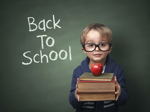 Boy with books and apple in front of chalkboard reading 'Back To School'