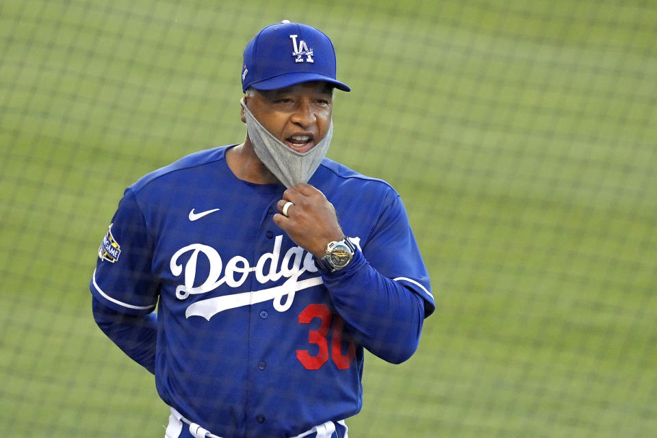 FILE - In this July 8, 2020, file photo, Los Angeles Dodgers manager Dave Roberts pulls down his mask to talk to someone in the dugout during an intrasquad baseball game in Los Angeles. Baseball is back, but because of the coronavirus, official scorers will work remotely this season to rule on hits and errors, make other judgments and tabulate box scores. (AP Photo/Mark J. Terrill, File)