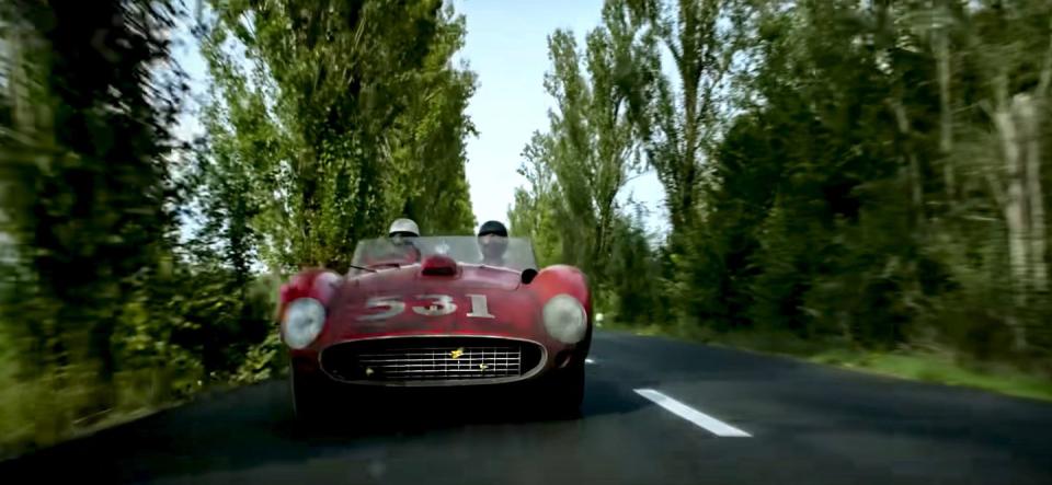 a vintage ferrari approaches the camera along a narrow tree lined road in a still from michael mann's upcoming film