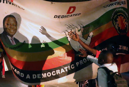 Zimbabweans celebrate next to a sign after President Robert Mugabe resigns in Harare, Zimbabwe November 21, 2017. REUTERS/Philimon Bulawayo