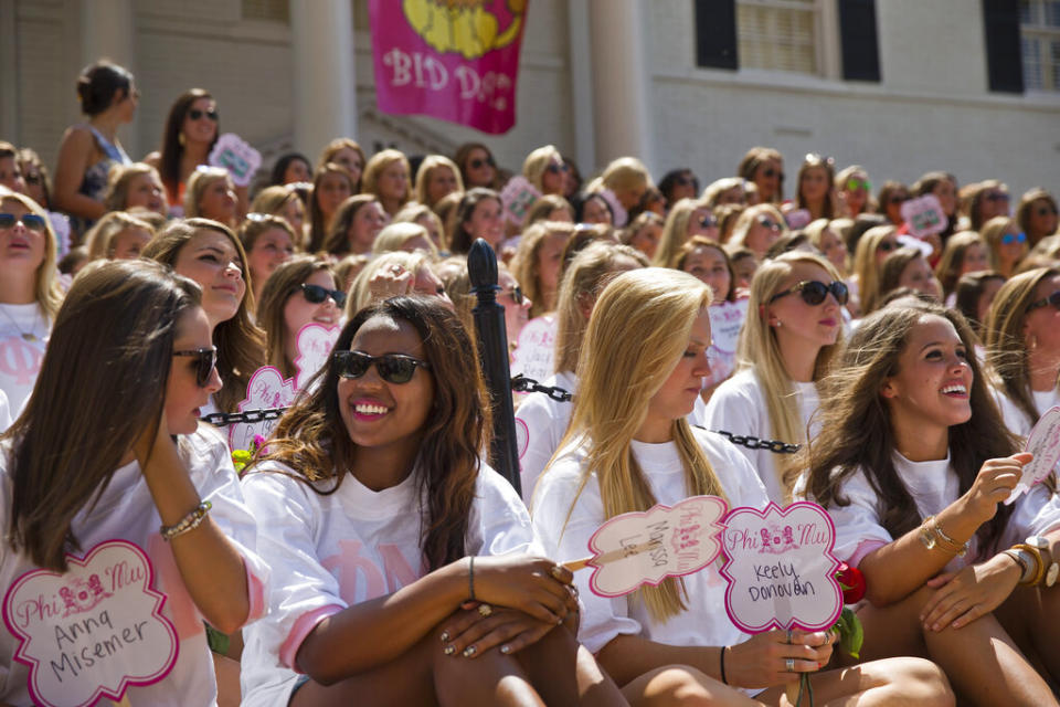 Young women sitting, smiling, and holding up signs with names on them