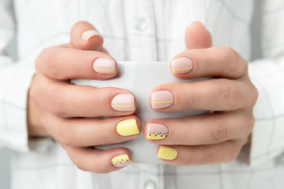 Manicured woman's hands holding a cup of coffee or tea. Spring summer yellow manicure design close up