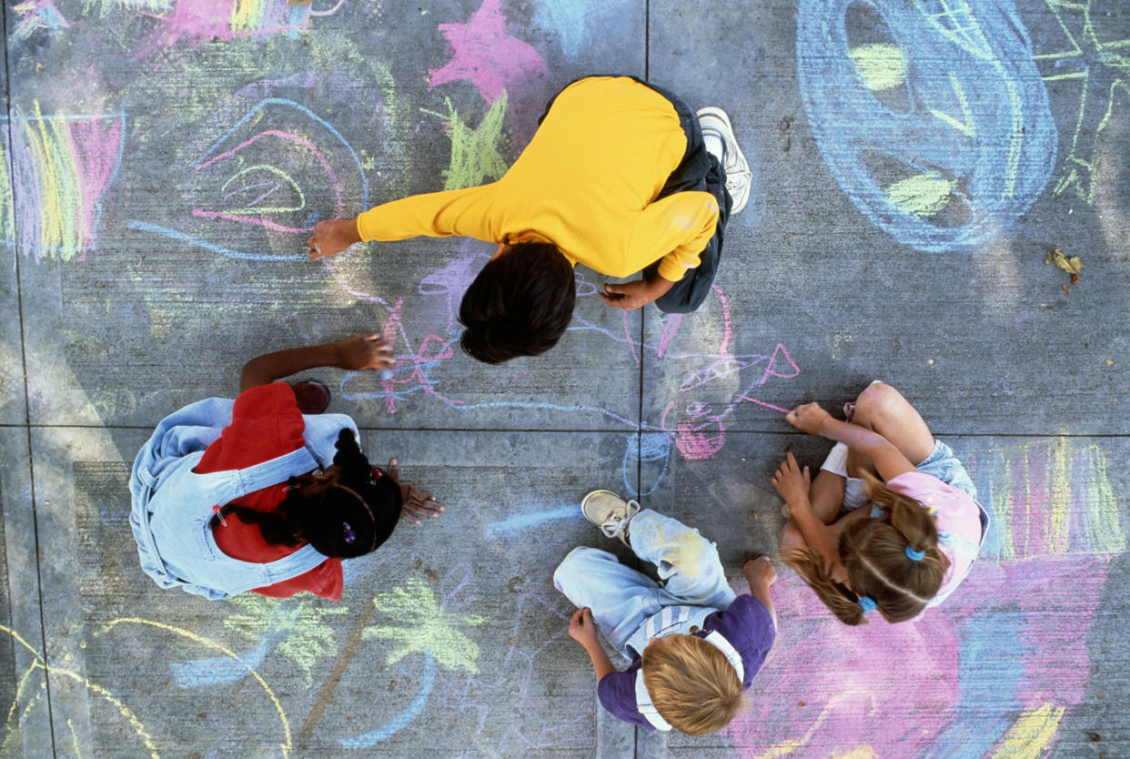 Four children drawing with chalk on pavement.