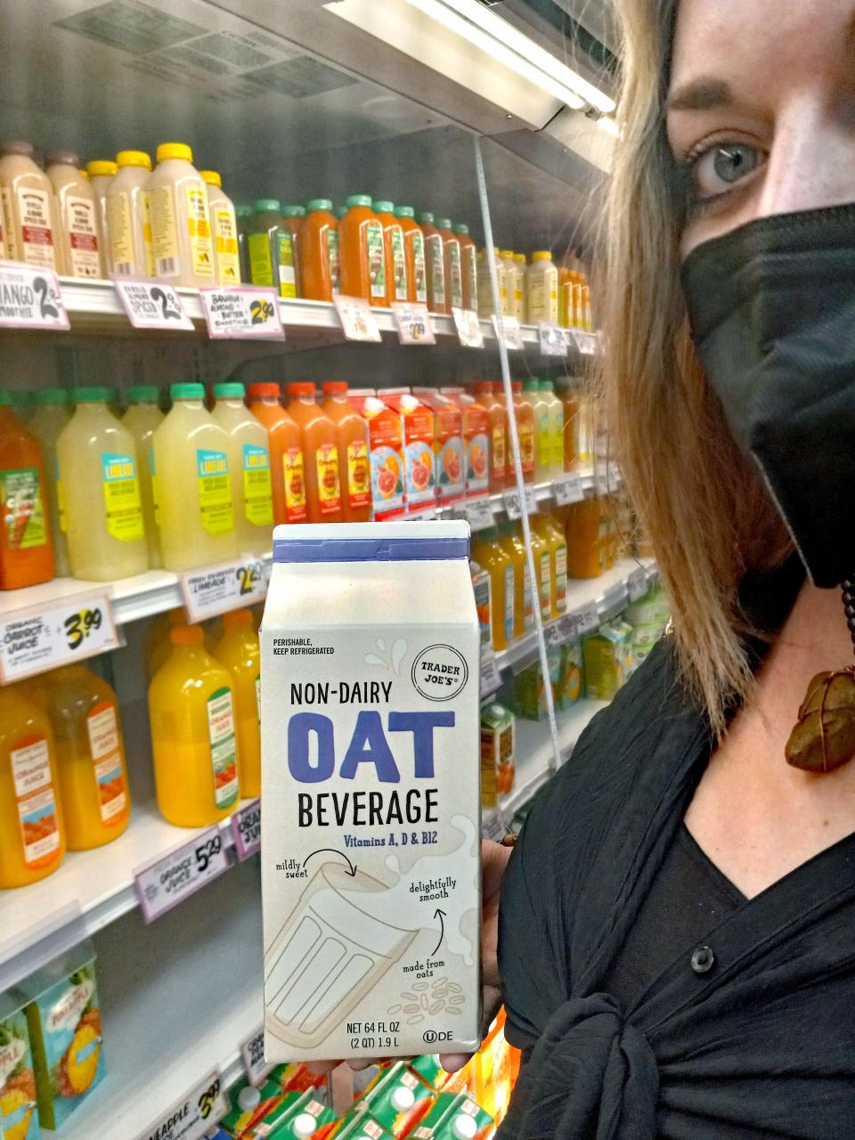 winter holding a carton of trader joe's oat milk in front of the beverage cooler